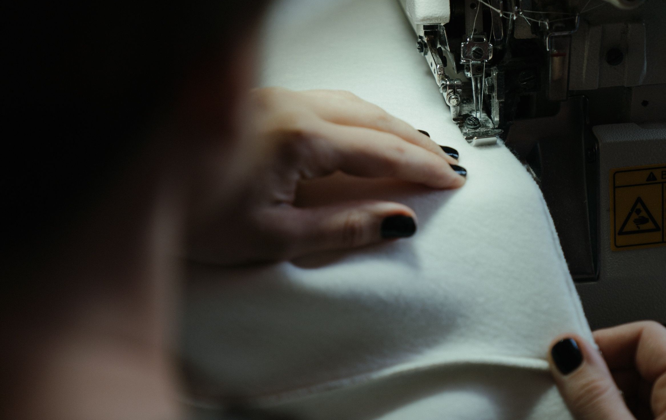 Hände führen weißen Stoff an einer Overlock-Nähmaschine - Fashion-grade Konfektion bei Atelierra Supply